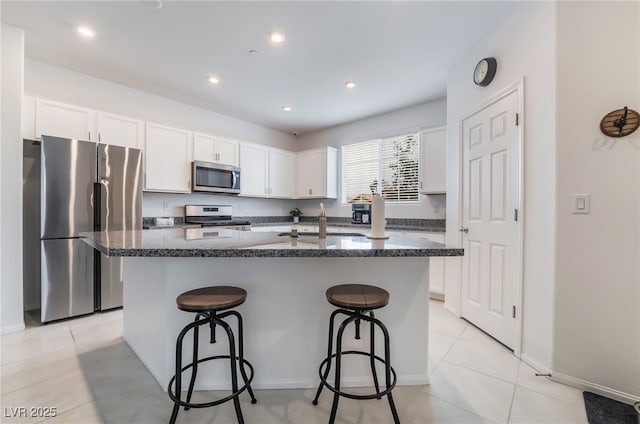 kitchen with light tile patterned floors, a center island with sink, a kitchen breakfast bar, stainless steel appliances, and white cabinetry