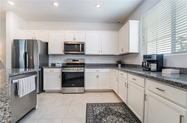 kitchen with dark stone countertops, appliances with stainless steel finishes, light tile patterned flooring, and white cabinets