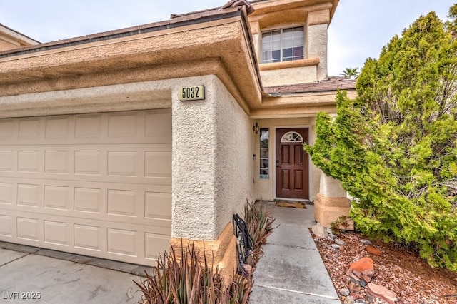 entrance to property featuring an attached garage and stucco siding