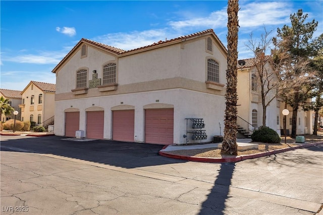 mediterranean / spanish house featuring a tiled roof, stucco siding, an attached garage, and driveway