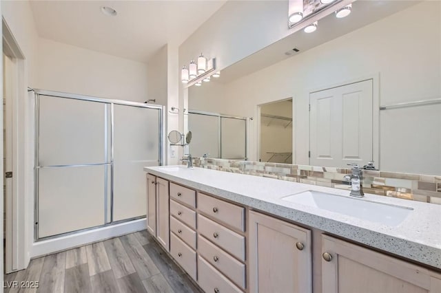 full bathroom featuring a stall shower, double vanity, a sink, and wood finished floors