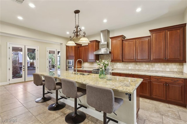 kitchen featuring tasteful backsplash, french doors, wall chimney range hood, a kitchen bar, and a sink