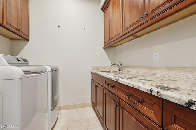 clothes washing area featuring light tile patterned floors, a sink, baseboards, cabinet space, and washing machine and clothes dryer