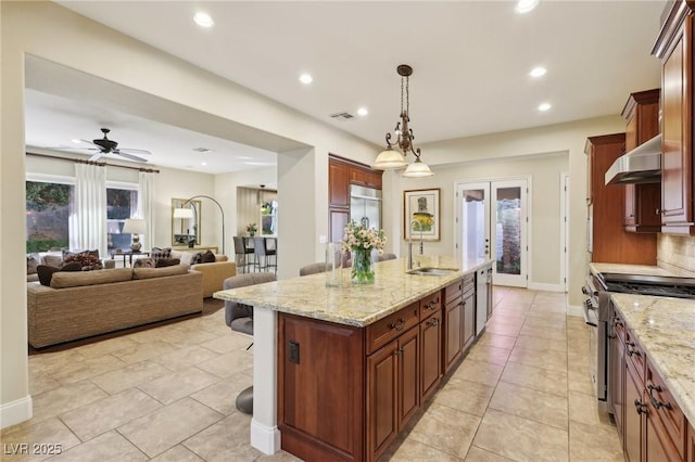 kitchen with a center island with sink, visible vents, high end appliances, wall chimney exhaust hood, and a sink