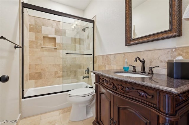 bathroom featuring tile walls, toilet, combined bath / shower with glass door, vanity, and tile patterned flooring