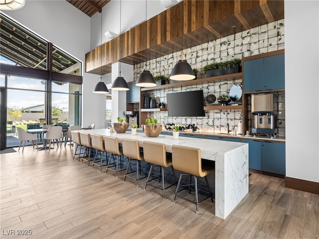 kitchen with a high ceiling, wood finished floors, a kitchen breakfast bar, decorative backsplash, and open shelves