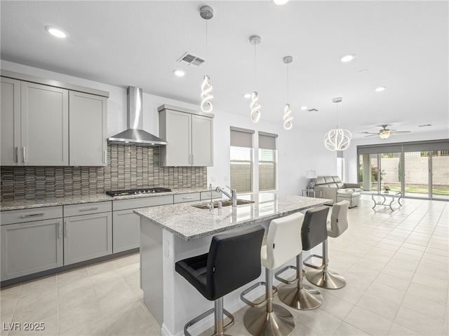 kitchen featuring gray cabinetry, a sink, visible vents, wall chimney exhaust hood, and stainless steel gas stovetop