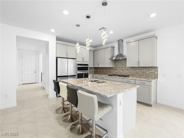 kitchen with decorative backsplash, appliances with stainless steel finishes, light stone counters, gray cabinetry, and wall chimney range hood