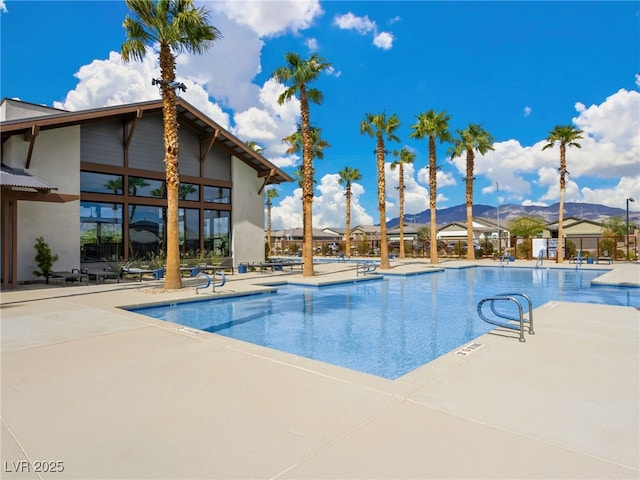 community pool with fence, a mountain view, and a patio