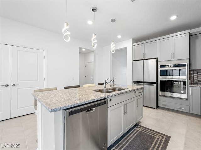 kitchen with light stone counters, stainless steel appliances, hanging light fixtures, gray cabinetry, and a sink