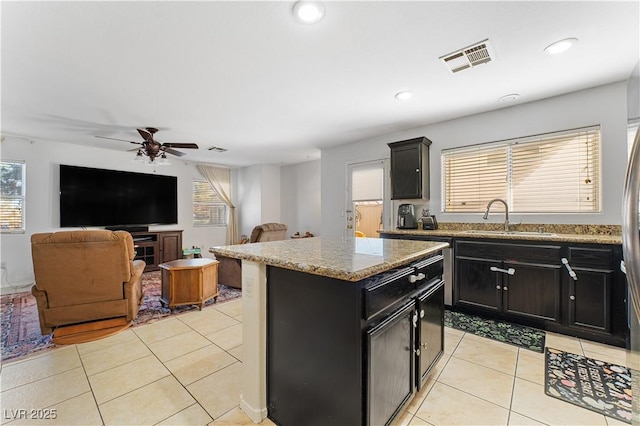 kitchen featuring visible vents, a sink, a center island, light tile patterned floors, and dark cabinets