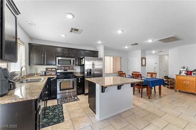 kitchen featuring visible vents, a kitchen bar, a sink, a kitchen island, and appliances with stainless steel finishes