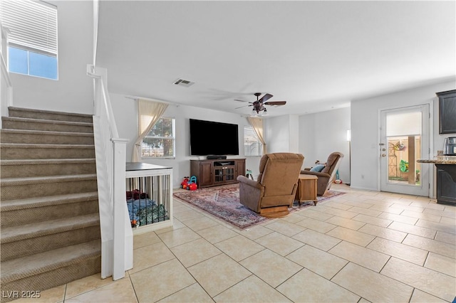 living area with light tile patterned floors, visible vents, a ceiling fan, and stairway