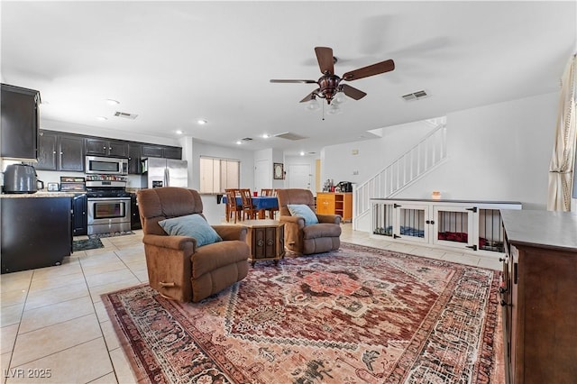 living room featuring stairway, light tile patterned floors, visible vents, and ceiling fan