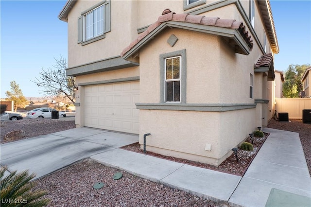 view of side of home with cooling unit, stucco siding, concrete driveway, a garage, and a tiled roof