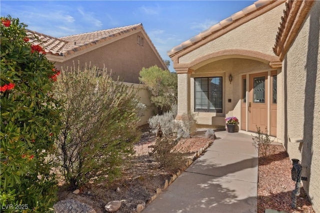 property entrance featuring fence, a tiled roof, and stucco siding