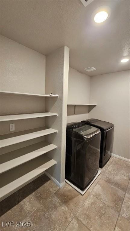 clothes washing area featuring laundry area, baseboards, a textured ceiling, and washing machine and clothes dryer