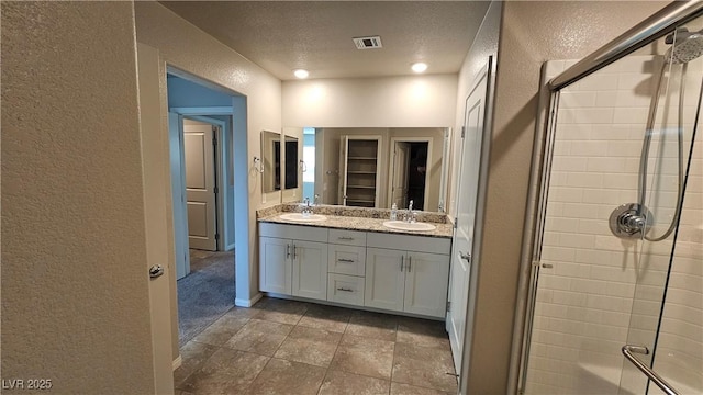 bathroom with a textured wall, a shower stall, a sink, and double vanity