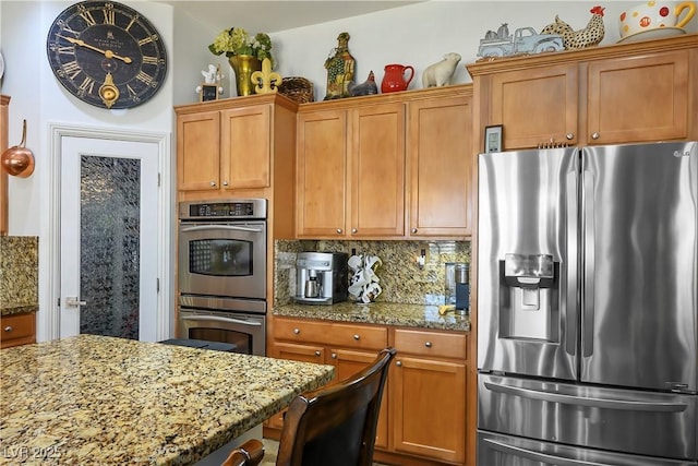 kitchen with brown cabinets, light stone countertops, stainless steel appliances, and backsplash