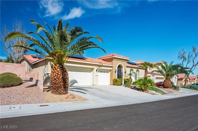 mediterranean / spanish-style house with driveway, solar panels, a tiled roof, and stucco siding