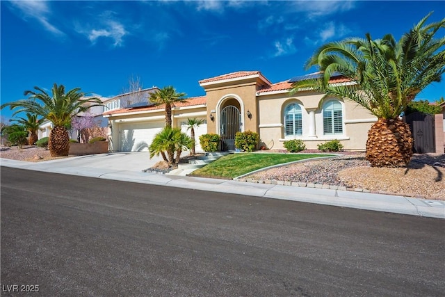 mediterranean / spanish-style house featuring driveway, a tile roof, an attached garage, roof mounted solar panels, and stucco siding