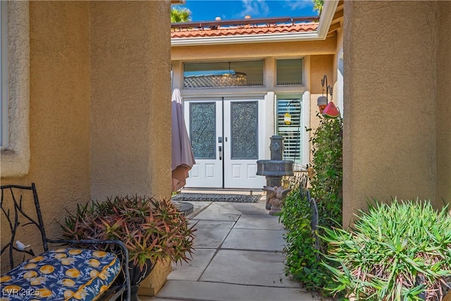 property entrance featuring a tiled roof, french doors, and stucco siding