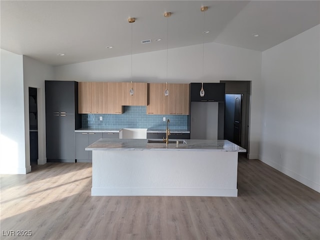 kitchen with vaulted ceiling, a sink, an island with sink, modern cabinets, and fridge