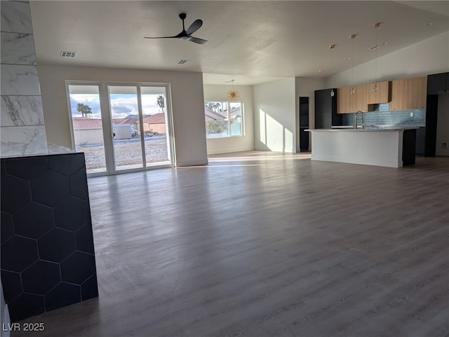 unfurnished living room with lofted ceiling, visible vents, a ceiling fan, a sink, and wood finished floors