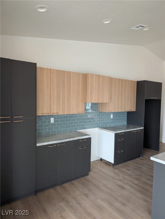 kitchen with vaulted ceiling, light countertops, decorative backsplash, light wood finished floors, and modern cabinets