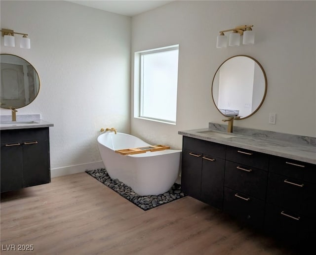 full bath with a freestanding bath, two vanities, a sink, and wood finished floors