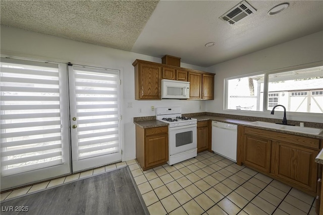 kitchen featuring white appliances, visible vents, dark countertops, a textured ceiling, and a sink