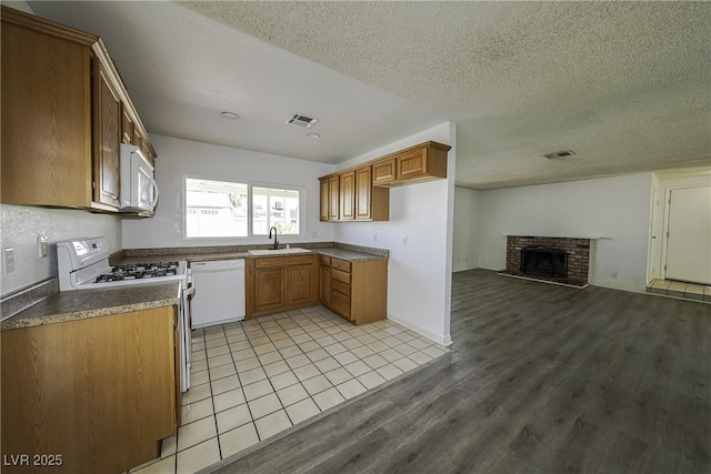 kitchen with white dishwasher, a sink, visible vents, range with gas stovetop, and brown cabinets