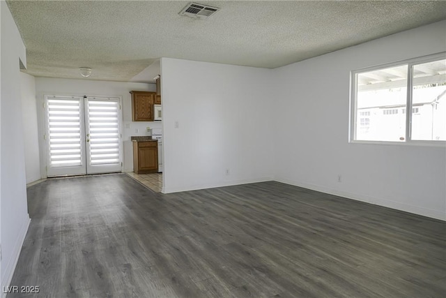 unfurnished living room featuring dark wood-style floors, visible vents, a textured ceiling, and baseboards