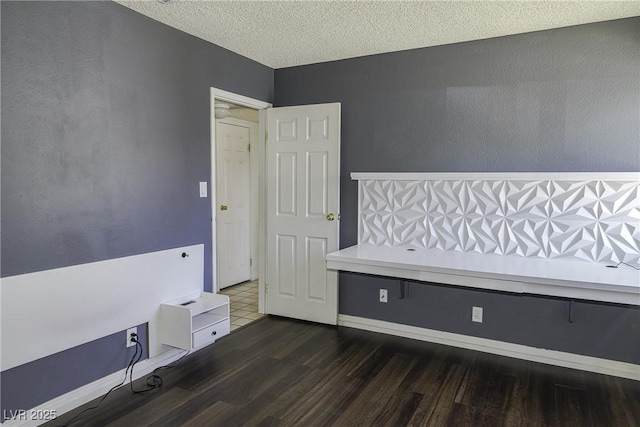 unfurnished bedroom with a textured ceiling, baseboards, and wood finished floors