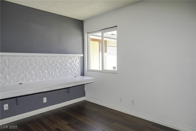 unfurnished room with a textured ceiling, dark wood-type flooring, and baseboards