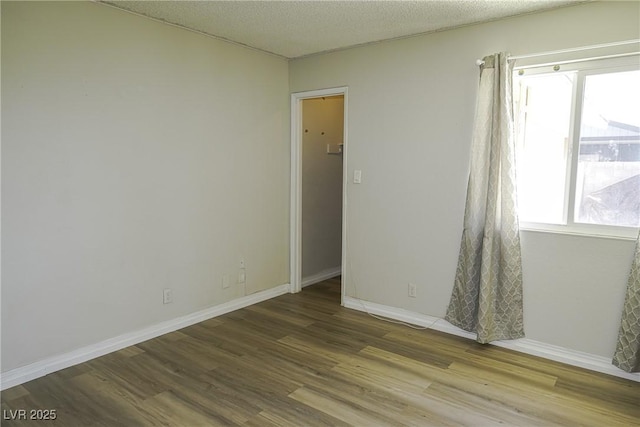 empty room with a textured ceiling, wood finished floors, and baseboards