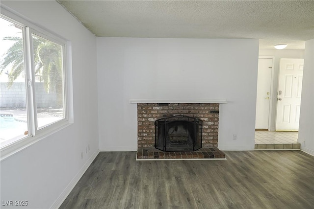 unfurnished living room featuring a textured ceiling, a fireplace, baseboards, and wood finished floors