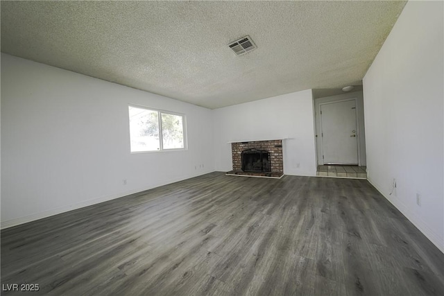 unfurnished living room with a brick fireplace, visible vents, a textured ceiling, and wood finished floors