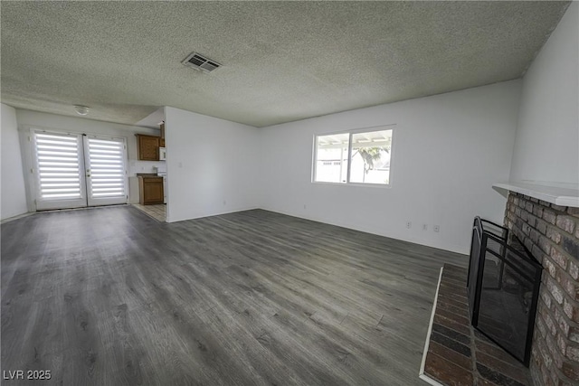 unfurnished living room with dark wood-type flooring, a brick fireplace, visible vents, and a textured ceiling