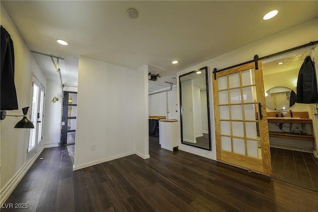 empty room with recessed lighting, wood finished floors, baseboards, and a barn door