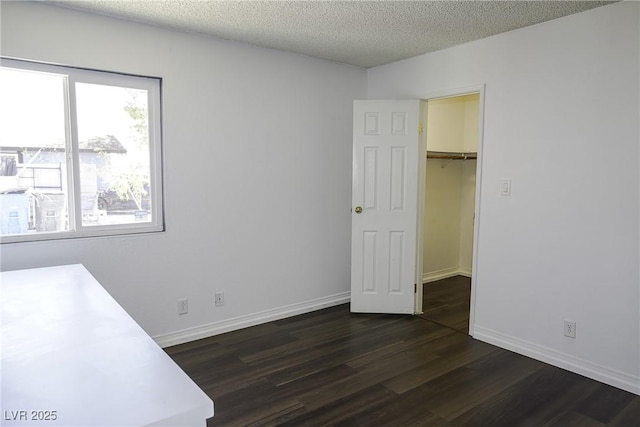 unfurnished bedroom featuring dark wood finished floors, a textured ceiling, baseboards, and a spacious closet