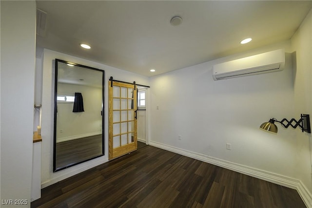 spare room featuring dark wood-style flooring, recessed lighting, a wall mounted AC, a barn door, and baseboards