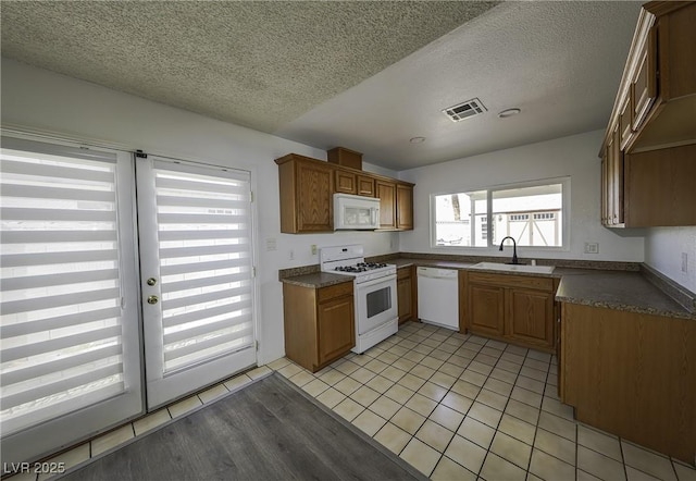 kitchen with white appliances, light tile patterned floors, visible vents, dark countertops, and a sink