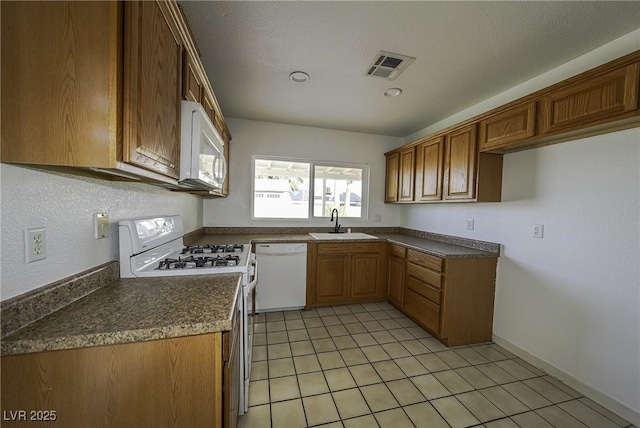 kitchen with light tile patterned floors, white appliances, a sink, visible vents, and brown cabinetry