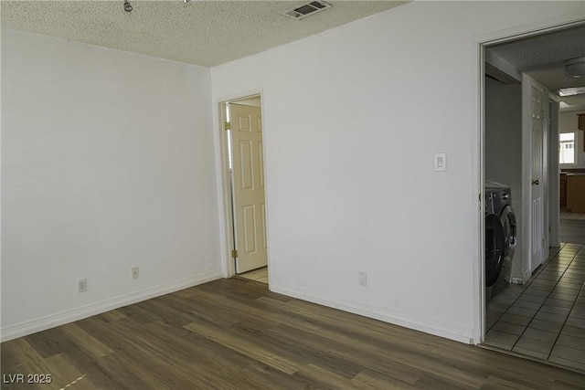 unfurnished room featuring a textured ceiling, separate washer and dryer, wood finished floors, visible vents, and baseboards