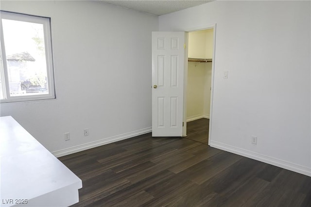 unfurnished bedroom with a closet, a spacious closet, dark wood-type flooring, a textured ceiling, and baseboards