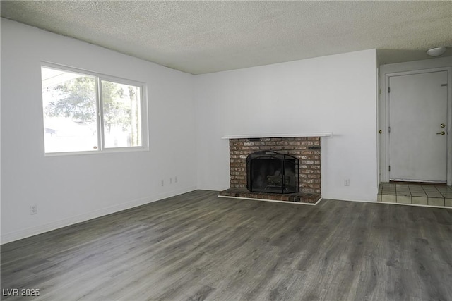 unfurnished living room with a textured ceiling, a brick fireplace, wood finished floors, and baseboards