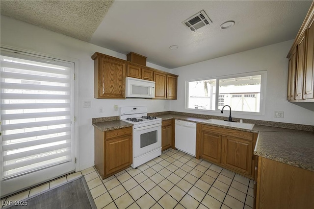 kitchen featuring dark countertops, visible vents, a sink, a textured ceiling, and white appliances