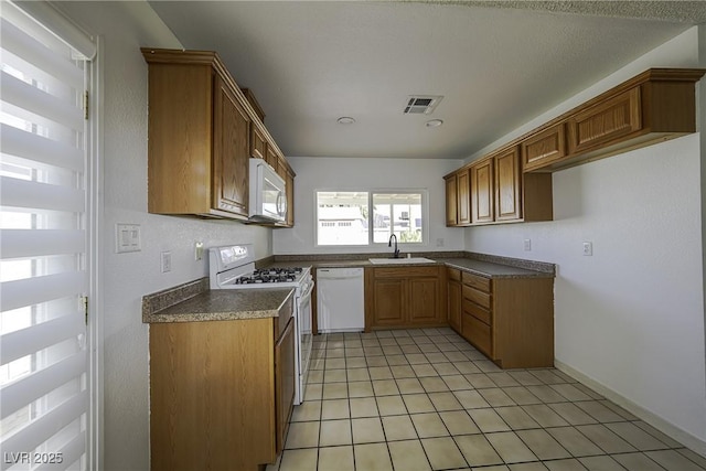 kitchen featuring light tile patterned floors, white appliances, a sink, visible vents, and brown cabinets