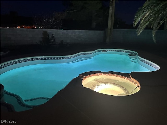 pool at twilight featuring fence private yard and a pool with connected hot tub